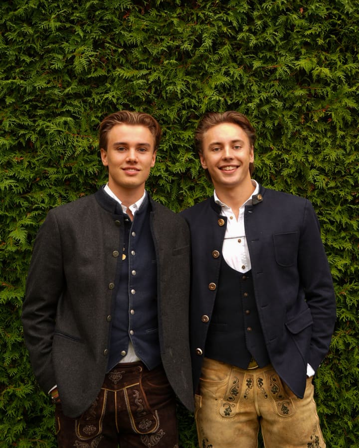 Julian Wüst (links) und Felix Praska, die Gründer von Feschwerk, in Trachtenjankern vor einer grünen Hecke
